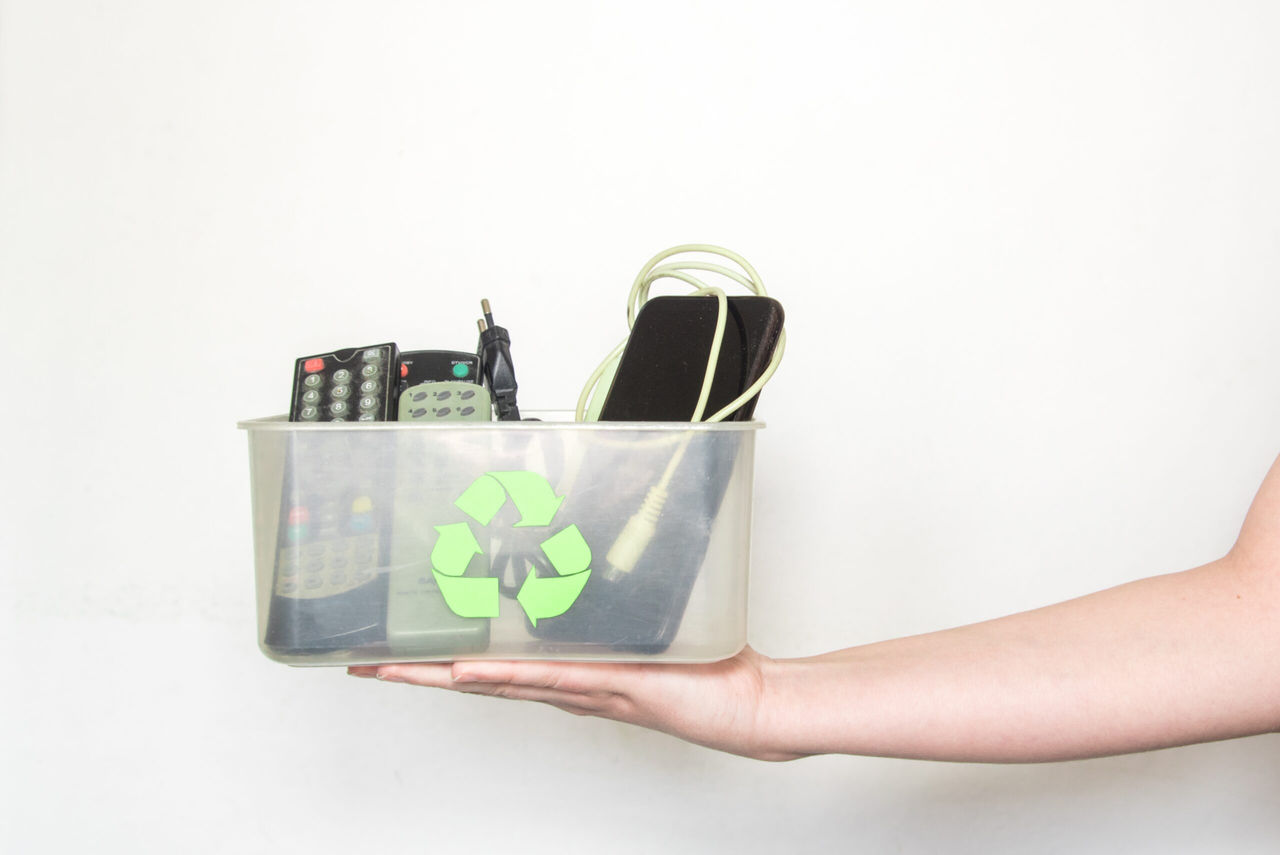 Mano sostiene objetos con elementos reciclados (Controles, cables, tablet,etc)