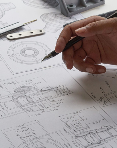 Mano realizando un dibujo técnico sobre planos de ingeniería con esquemas mecánicos y piezas industriales.
