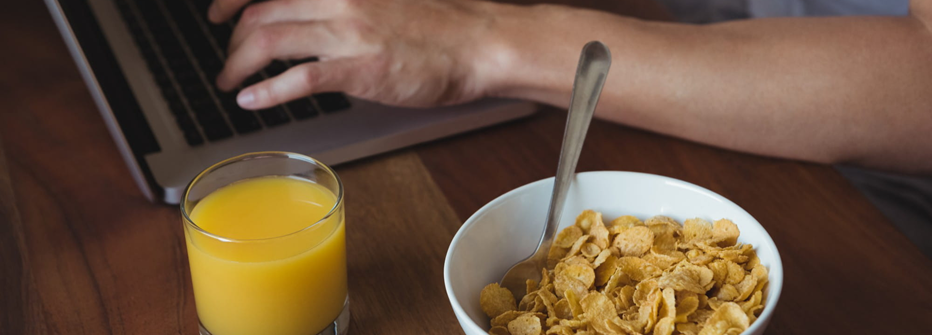 Manos escribiendo en una laptop al lado se percibe un tazón con cereal