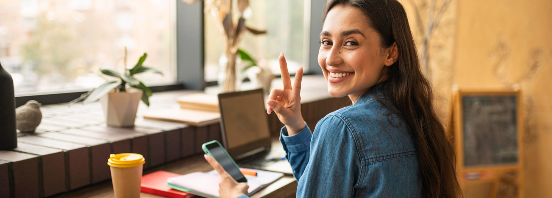 Mujer sonrie para la cámara, mientras responde correos y mensaje en su celular